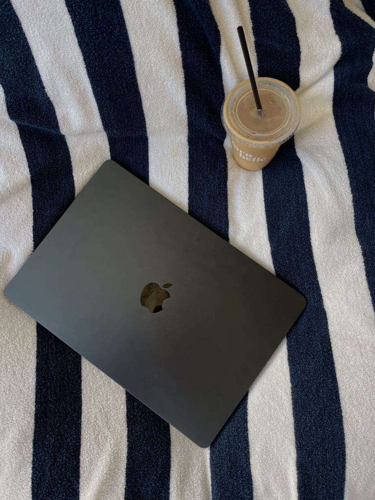 how to find clients for travel agency. Picture of a laptop and iced coffee on a towel.